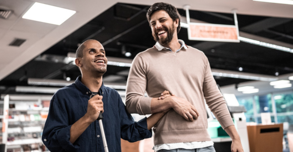 A man assists a blind man walking through a store